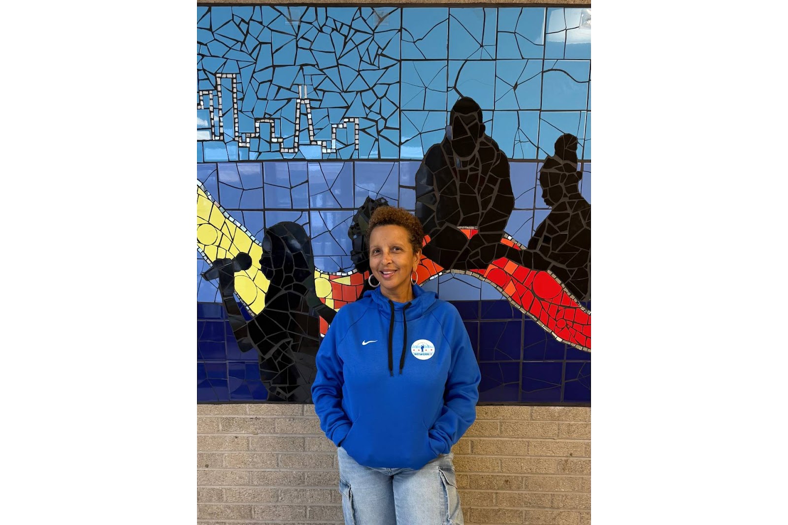 Ramona Outlaw, Administrator-in-Charge at Harlan Community Academy, smiling in front of a colorful stained glass mural.